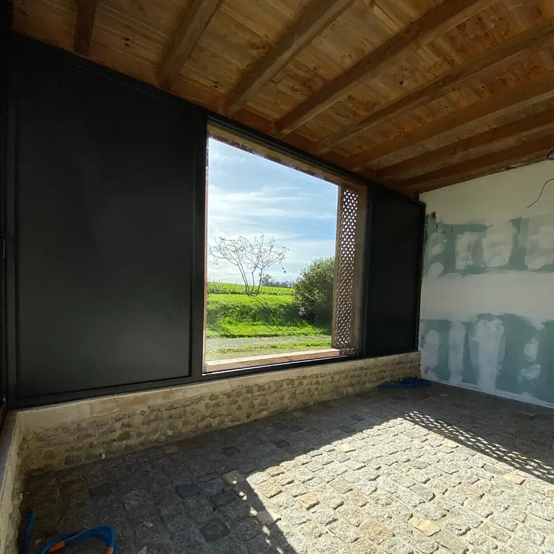 Partie vitrée fixe encadrée de deux panneaux pleins noirs, dans la dépendance aux murs encore en plaques de plâtre