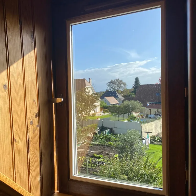 Fenêtre à cadre ton bois dans une pièce lambrissée, avec vue sur les toits et les jardins