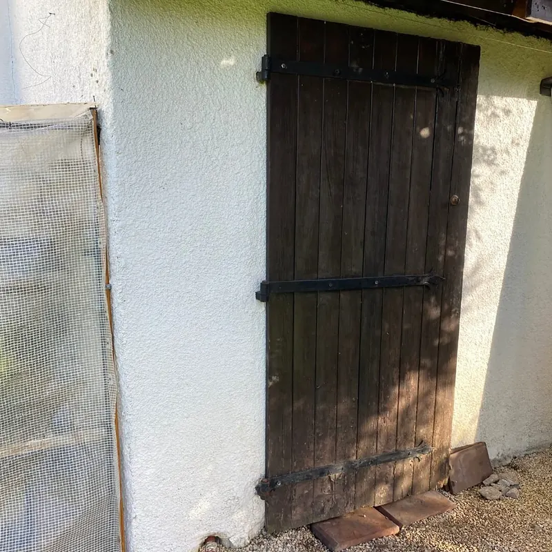 Avant : Ancienne porte en planches de bois sombre sur le mur blanc de l’abri, avant son remplacement