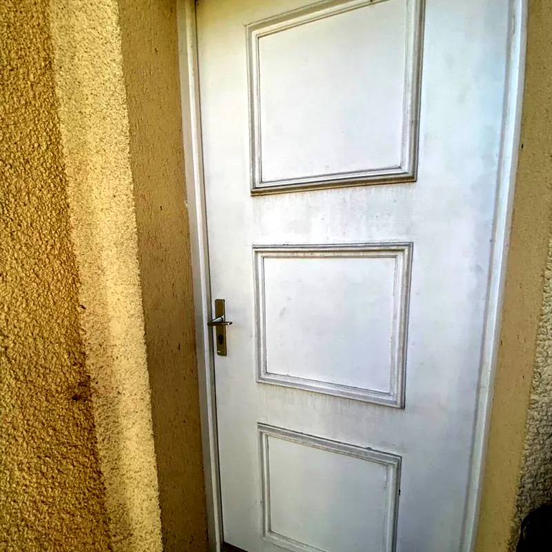Avant : Ancienne porte d’entrée blanche à trois panneaux moulurés, avant son remplacement