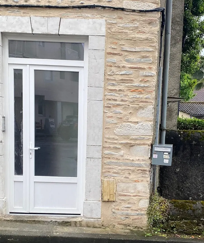 Porte d’entrée PVC blanche vitrée avec imposte, posée dans un encadrement en pierre de taille sur une façade en galets